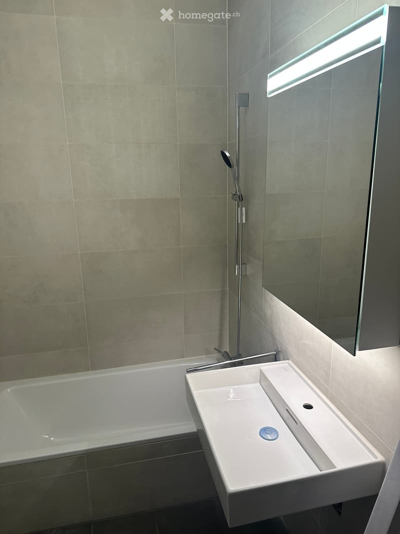 Modern bathroom with a white bathtub, a double sink, a chrome faucet, and a large mirror with a built-in light strip.