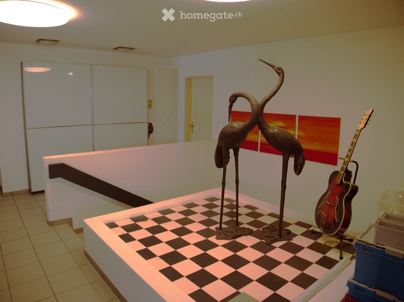 A modern, well-lit room with a checkered floor, featuring a large guitar and two tall bird sculptures, along with a painting on the wall.