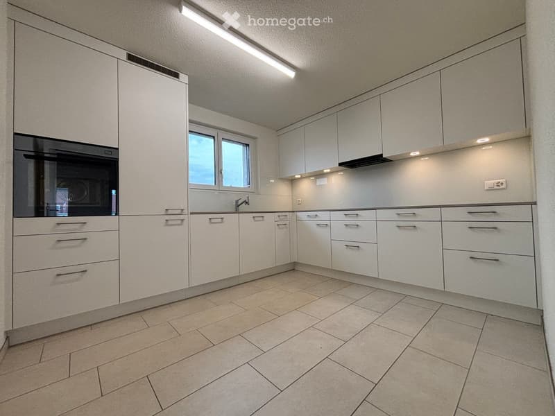 Modern kitchen with white cabinets, tiled floor, and a window above the sink.