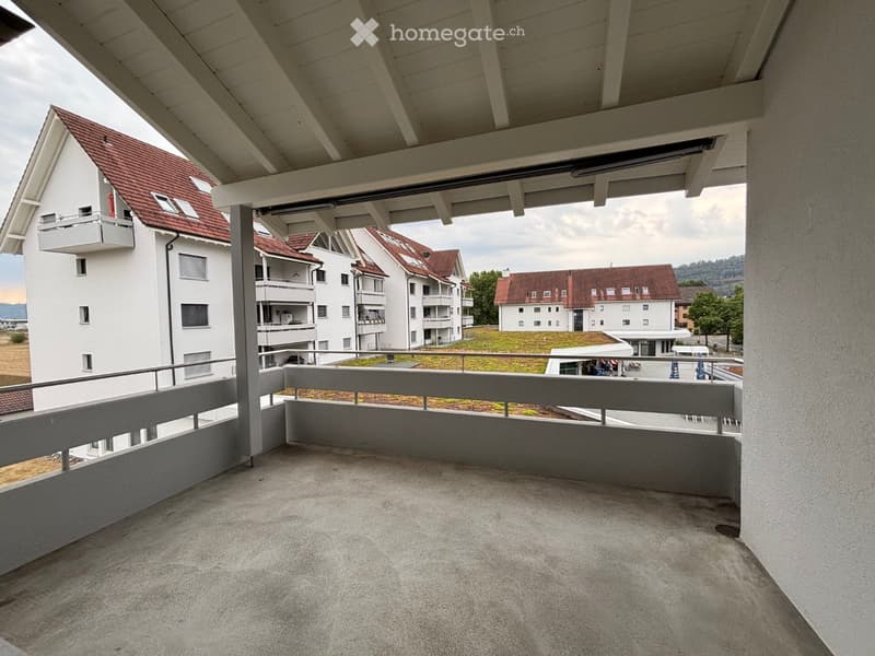 Empty balcony with concrete floor, metal railing, and a view of surrounding buildings and greenery.