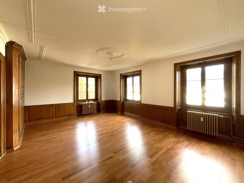Empty room with wooden flooring, large windows, and radiators along the walls. No furniture or furnishings are present.
