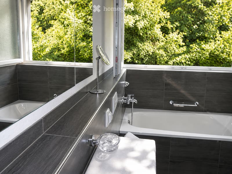 Modern bathroom with dark tiled walls, a bathtub, a mirror, and a towel on the counter.
