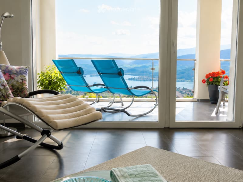 Balcony with lounge chairs, a small table, and a flower pot, offering a scenic view of a lake and mountains.