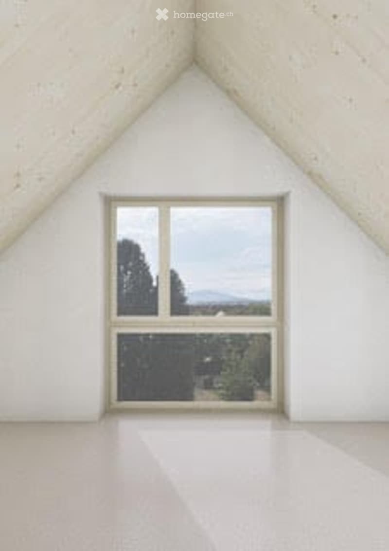 Empty attic room with slanted white walls, large window offering a scenic view of trees and mountains.