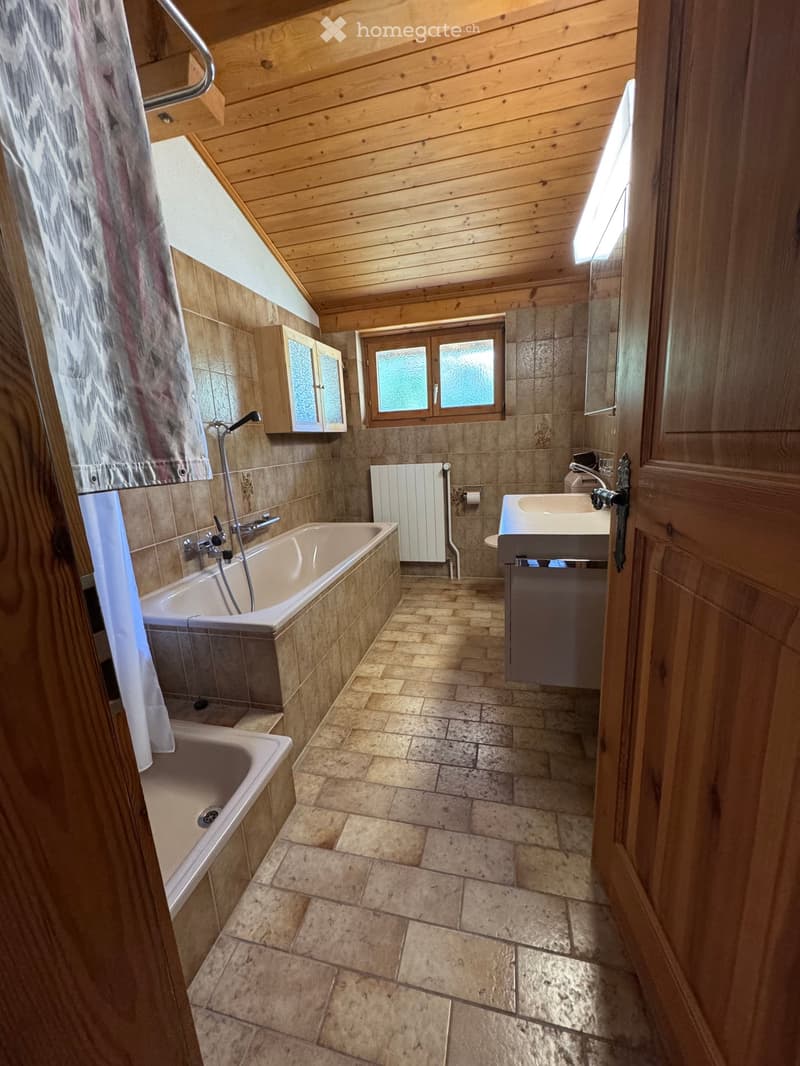 Bathroom with wooden ceiling, tiled walls, bathtub, sink, mirror, radiator, and cabinet.