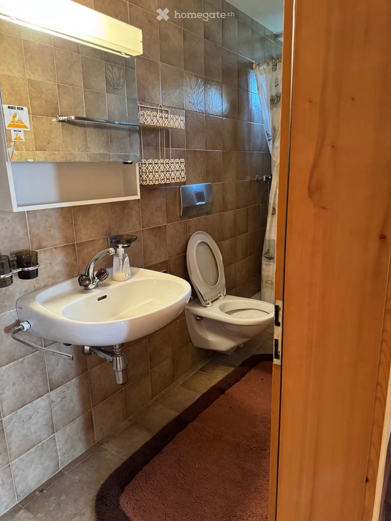 Bathroom with a white sink, chrome faucet, toilet, mirror, towel rack, and a shower curtain visible in the background.