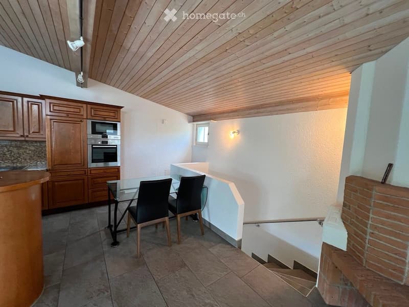 Bright kitchen with wooden cabinets, stainless steel appliances, a glass dining table with two black chairs, and a small window.