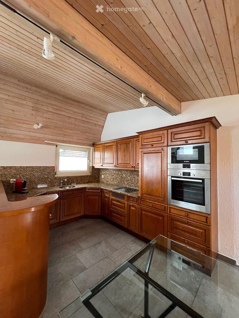 Modern kitchen with wooden cabinets, stainless steel oven, granite countertops, and a glass table.