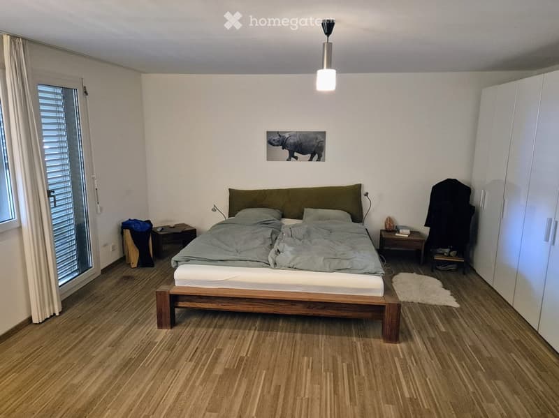 Modern bedroom with wooden flooring, a large bed with grey bedding, nightstands, a picture frame on the wall, and a white wardrobe.