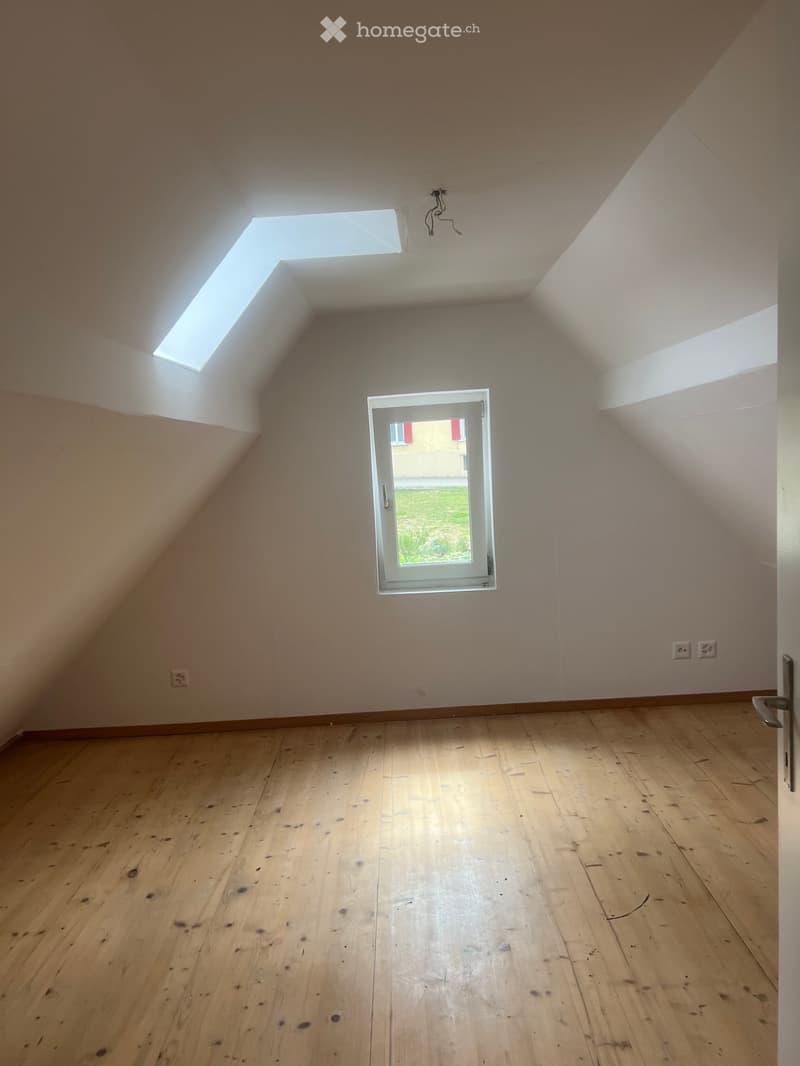 Empty attic room with wooden flooring, slanted ceilings, skylight windows, and a door leading outside.
