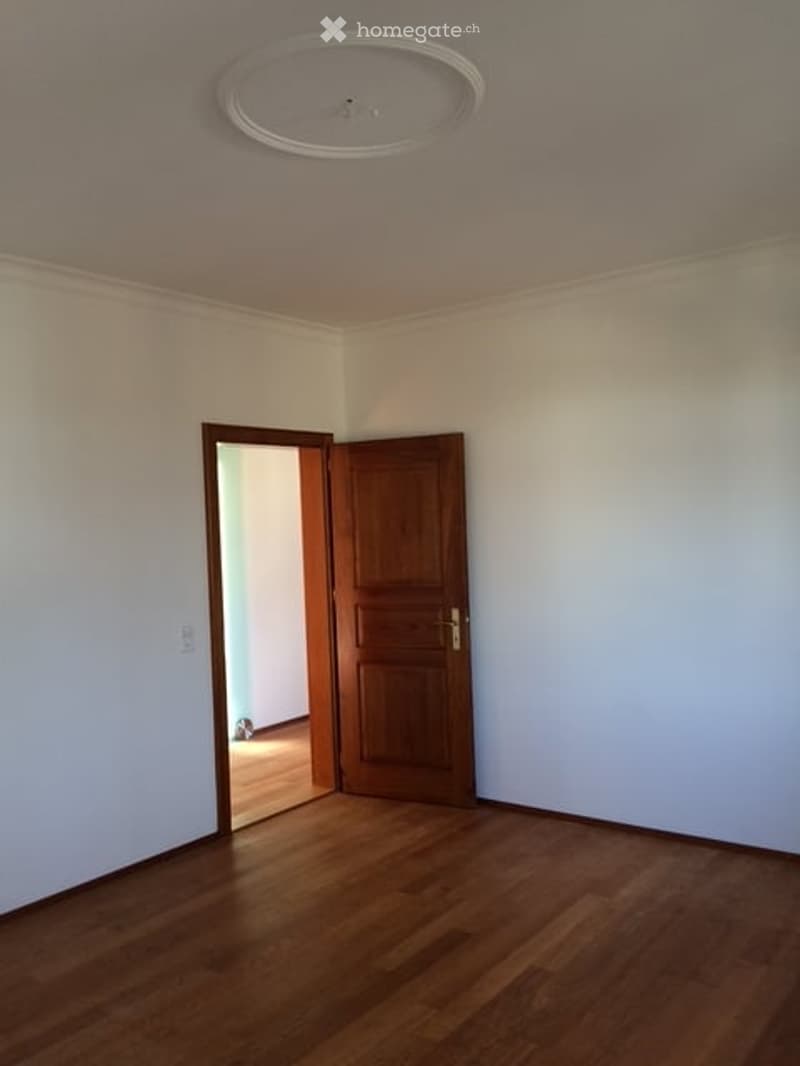 Empty room with light-colored walls, wooden flooring, and a single wooden door leading to another space.