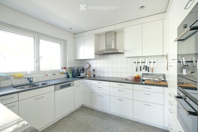 Modern kitchen with white cabinets, stainless steel appliances, and a black countertop. Features include a sink, dishwasher, coffee maker, oven, range hood, and various kitchen utensils.