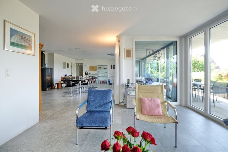 Modern living room with large windows, fireplace, sofa, chairs, dining area, and artwork on the walls.