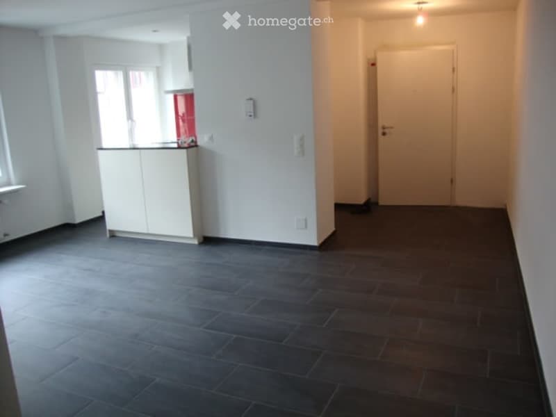 Empty room with white walls, dark tiled floor, white cabinet, and a window with blinds.