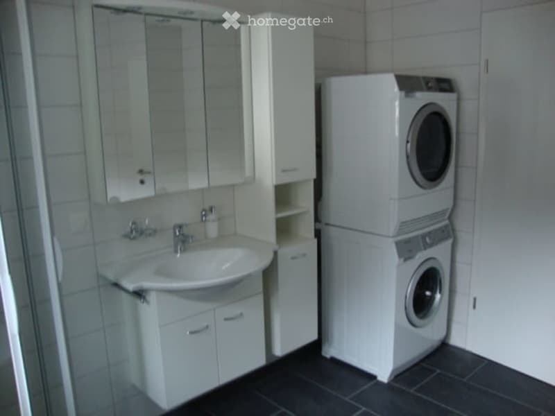 Modern bathroom with white tiles, a sink with a mirror cabinet, and a stacked washer/dryer unit.