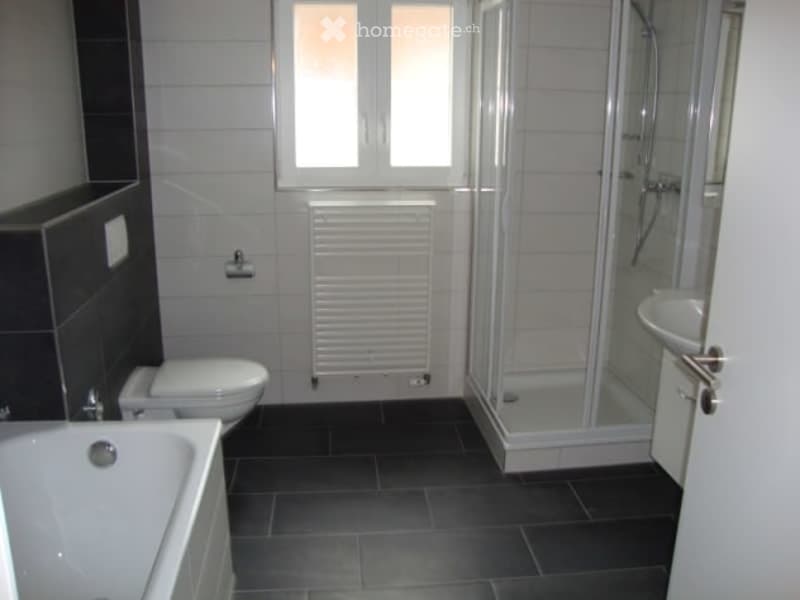 Modern bathroom with a bathtub, toilet, shower, sink, and radiator. The floor is tiled in dark gray, and the walls are white with a dark accent wall.