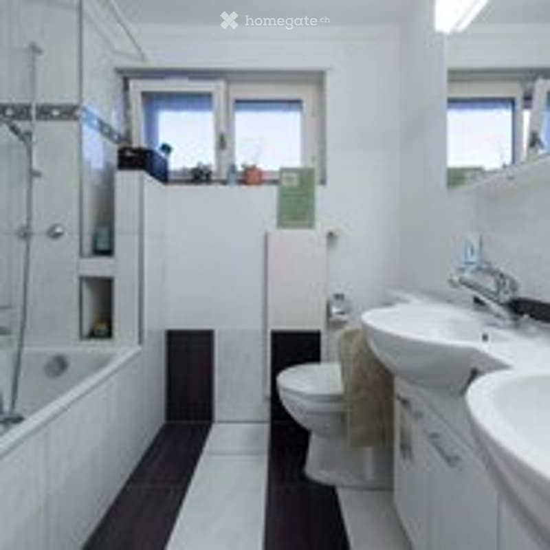 Modern bathroom with white tiles, black accents, a toilet, two sinks, a shower, and a mirror above the sink.
