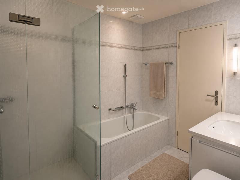 Modern bathroom with a bathtub, glass shower enclosure, sink, toilet, and a towel on a rack.