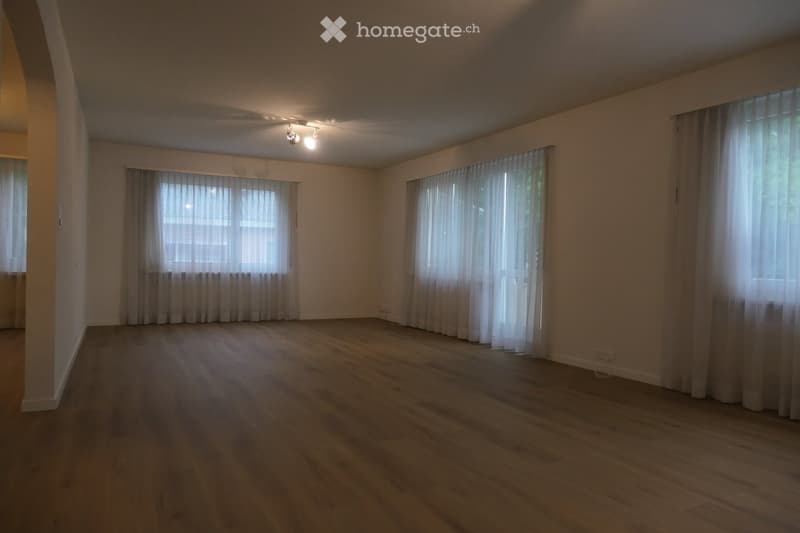 Empty room with wooden flooring, white walls, and large windows covered with sheer curtains. No furniture or equipment present.
