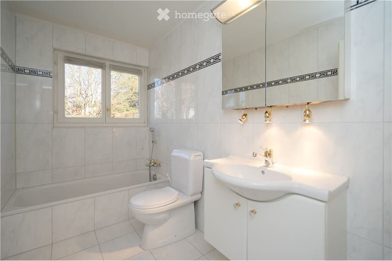 Modern bathroom with white tiles, a bathtub, toilet, sink, and a large mirror with built-in cabinets.