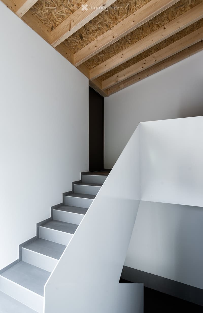 Modern staircase with grey steps and white walls, featuring a wooden ceiling with exposed beams and insulation.