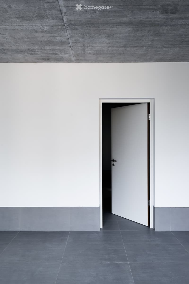 Empty room with grey tiled floor, white walls, and a partially open white door leading to another space.