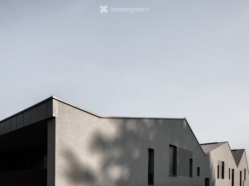 Modern, minimalist building with a textured concrete facade, geometric roofline, and small windows.