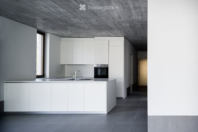 Modern kitchen with white cabinets, a central island, a sink, a faucet, and an oven. The space features a concrete ceiling and dark tiled flooring.