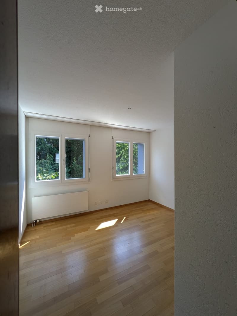 Empty room with wooden flooring, white walls, and large windows allowing natural light. No furniture or equipment present.
