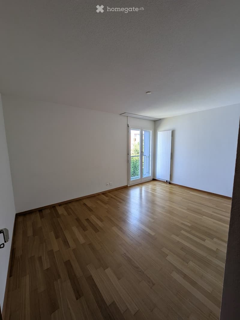 Empty room with wooden flooring, white walls, and a sliding glass door leading to a balcony.