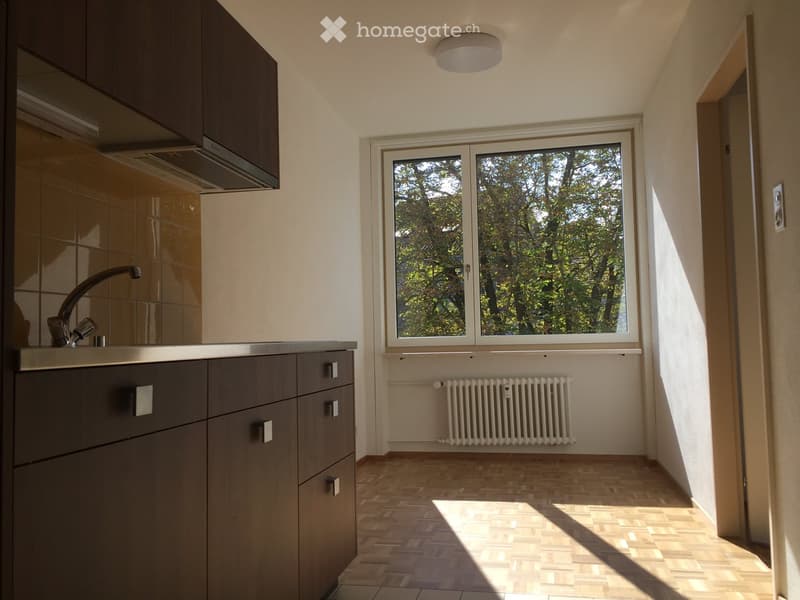Modern minimalist kitchen with wooden cabinets, stainless steel countertops, tile backsplash, large window, and radiator