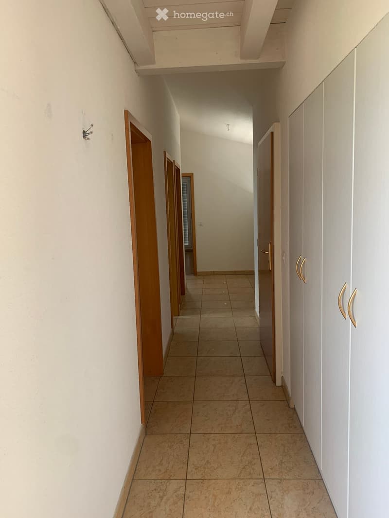 Empty hallway with tiled floor, white walls, and wooden doors on both sides.