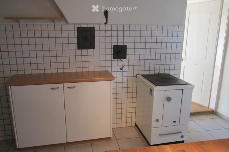 Small kitchen with white tiled walls, wooden countertop, white cabinets, and a built-in electric stove.