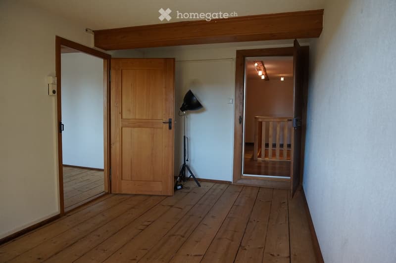 Empty wooden-floored hallway with two open doors leading to other rooms, a floor lamp, and a visible staircase in the background.