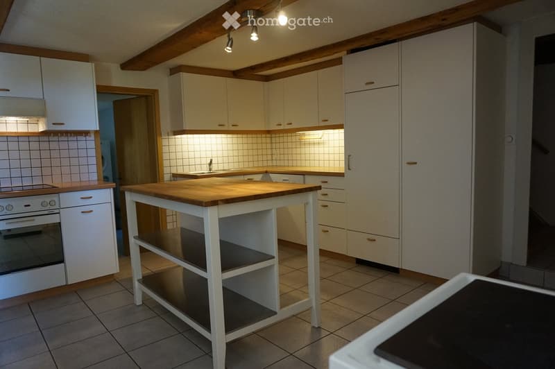 Bright kitchen with white cabinets, wooden island, tiled backsplash, and built-in oven.