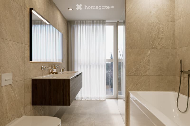 Modern bathroom with a double sink vanity, large mirror, bathtub, and a view through sheer curtains.