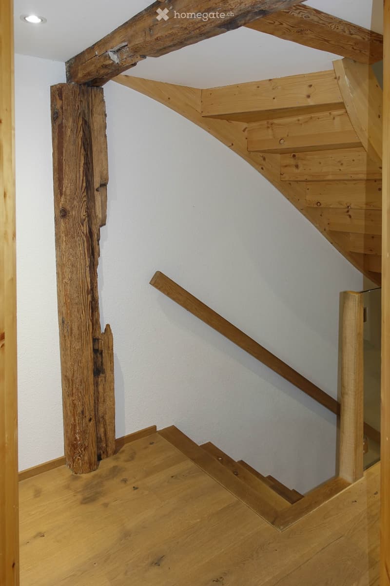 Wooden staircase with a rustic wooden post and handrail, leading upwards with a modern recessed ceiling light.