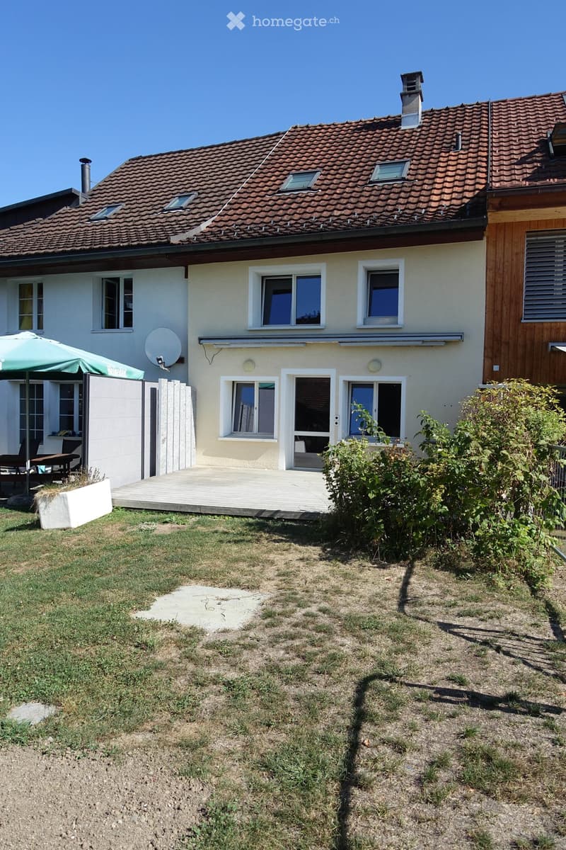 Two-story house with a red-tiled roof, multiple windows, and a small patio area with outdoor furniture.