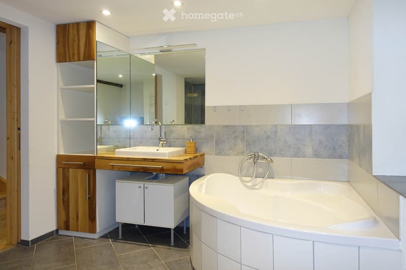 Modern bathroom with a white bathtub, wooden vanity with sink, mirrored cabinet, and tiled walls.
