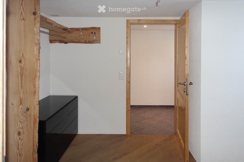 Empty hallway with wooden flooring, white walls, and a partially open wooden door leading to another room.