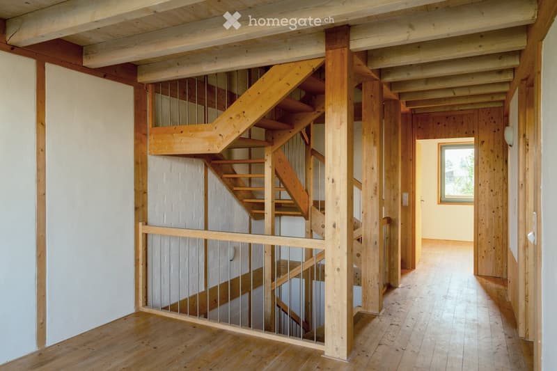 Wooden staircase with metal railing, wooden floor, white walls, and exposed wooden beams on the ceiling.