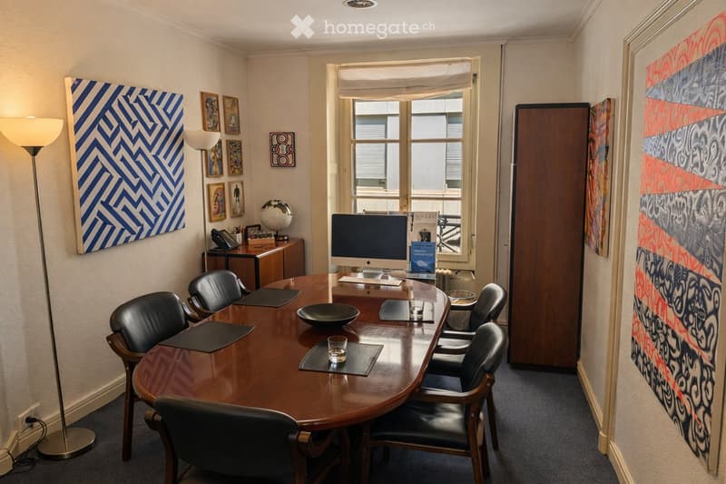 Conference room with a large wooden table, black chairs, computer, floor lamp, framed artwork, globe, and telephone.
