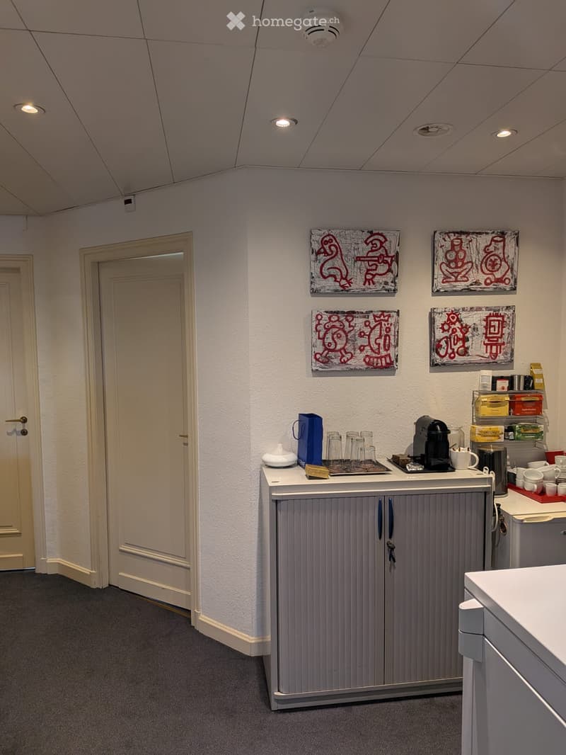 A small break room with a grey cabinet, coffee machine, cups, and a small counter area.