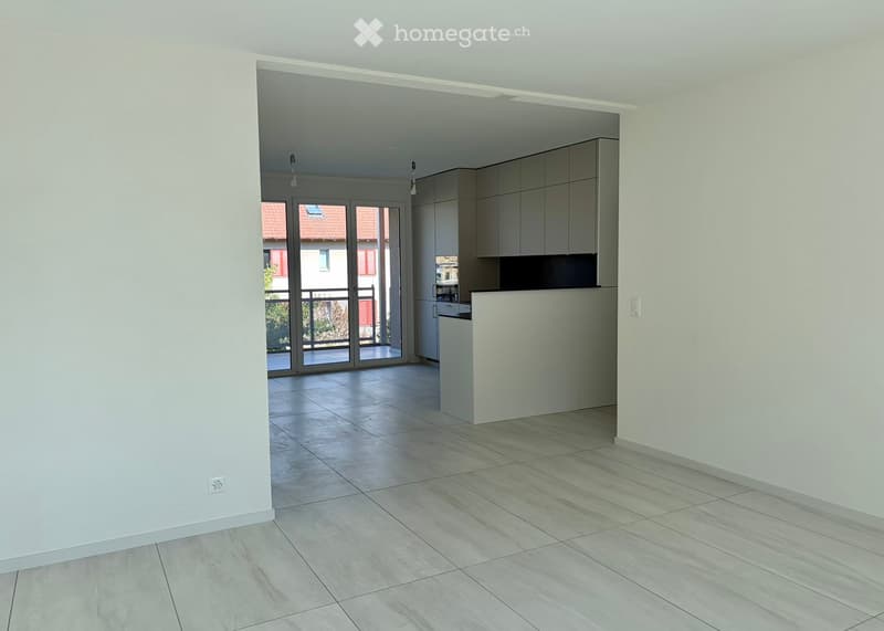 Open-plan living and kitchen area with modern grey cabinets, white countertop, tiled flooring, and large sliding glass doors leading to a balcony.