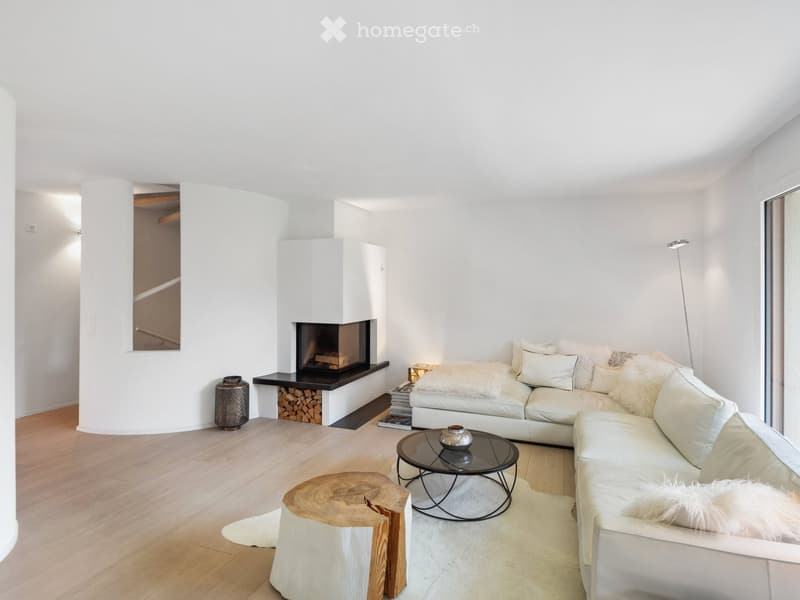 Modern living room with white walls, light wood flooring, a white sectional sofa, a black coffee table, a wooden stool, a fireplace, and a floor lamp.