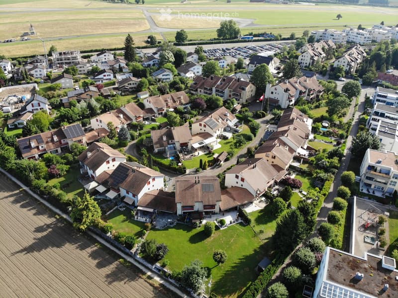 Aerial view of a residential neighborhood with multiple houses, gardens, and surrounding greenery.