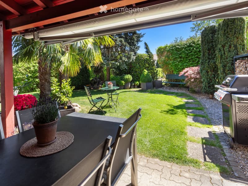 Well-maintained garden with a patio area, outdoor dining table, chairs, potted plants, a barbecue, and a neatly trimmed lawn.