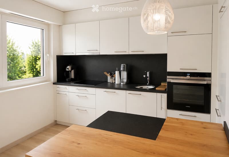 Modern kitchen with white cabinets, black countertops, and stainless steel appliances. Features a coffee maker, oven, sink, and various kitchen utensils.