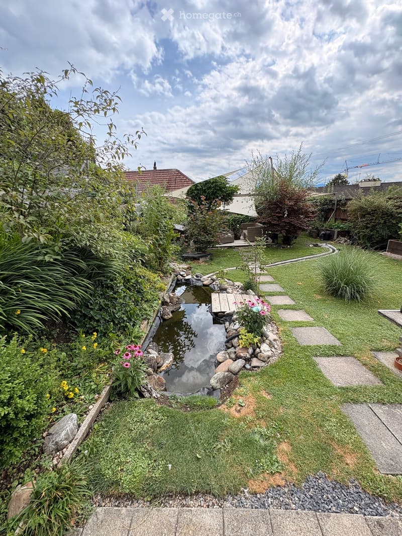 Well-maintained garden with a small pond, stepping stones, lush greenery, and colorful flowers.