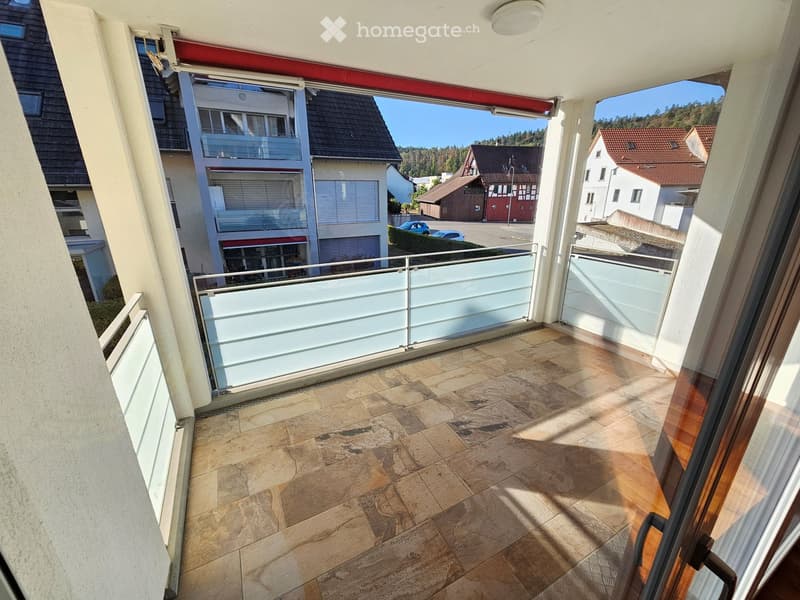 Balcony with tiled floor, glass railing, and view of surrounding buildings and greenery.